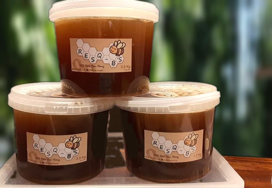 Three 3.5 kg buckets of RESQ-B'S raw honey stacked in a pyramid, each with the honeycomb label
